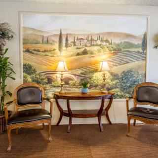 A cozy seating area featuring two chairs and a table, flanked by lamps, with a mural of a scenic landscape in the background.