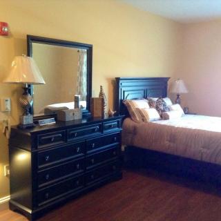 A cozy bedroom featuring a bed with pillows, a dark wooden dresser with a mirror, and two lamps.