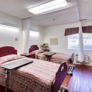A spacious patient room in a healthcare facility, featuring two beds and natural light from a window.