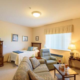 A cozy bedroom with a bed, armchair, and sofa arranged near a window.