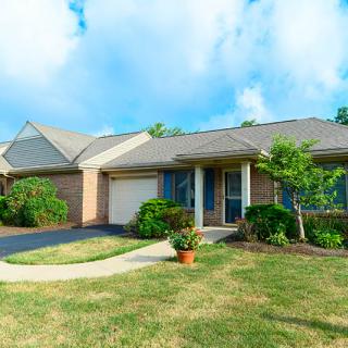 A suburban house with a front yard and driveway under a partly cloudy sky.