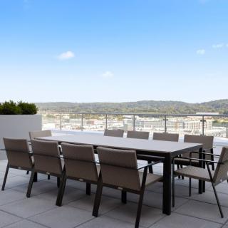 A spacious outdoor patio with a large table and chairs, offering a scenic view of hills under a clear blue sky.