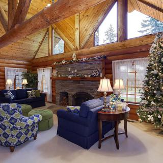 A cozy log cabin living room with wooden beams, a decorated Christmas tree, and a warm fireplace.