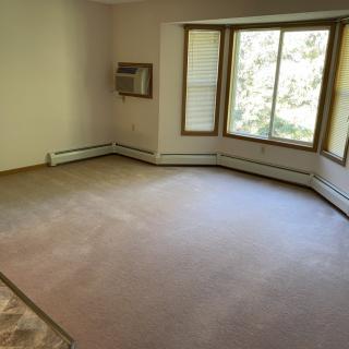 A spacious empty room with carpet, large windows, a baseboard heater, and an air conditioning unit.