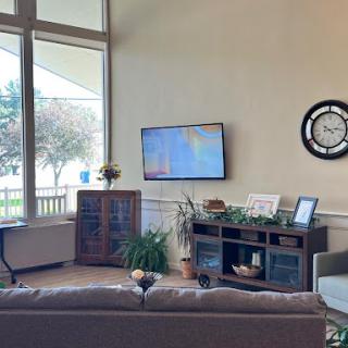 A cozy living room with a modern aesthetic, featuring a television and decorative plants near large windows.