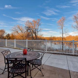 A peaceful patio overlooking a lake with a table and chairs set against a backdrop of autumn trees under a clear blue sky.