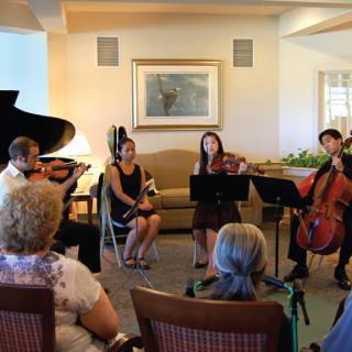 A chamber music group performs for an intimate audience in a cozy indoor setting.