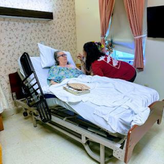 A caregiver assists a patient in a hospital room, providing comfort and care.