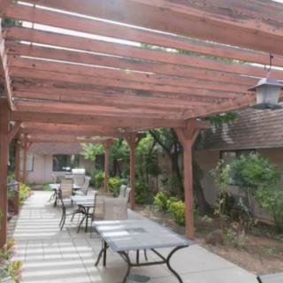 A peaceful patio area with a pergola overhead, featuring tables and chairs surrounded by greenery.