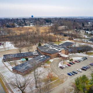An aerial view of a school campus surrounded by trees and a parking lot, captured during winter.