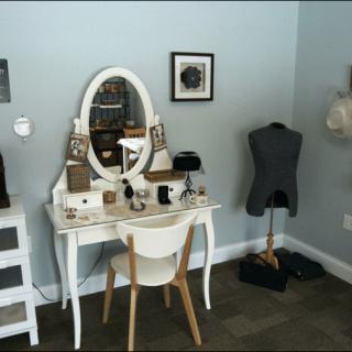 A stylish vanity setup with a mirror, chair, and decorative items next to a mannequin.
