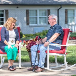 Two people sitting on red chairs having a conversation in a garden setting.