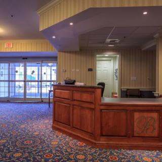 A hotel lobby with a wooden reception desk and colorful carpet.