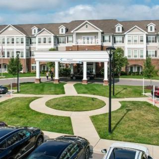 A large residential building with white columns at the entrance, surrounded by well-maintained landscaping and a parking lot.