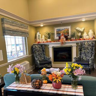 A cozy living room adorned with autumn decorations and fresh flowers, featuring comfortable seating by the fireplace.