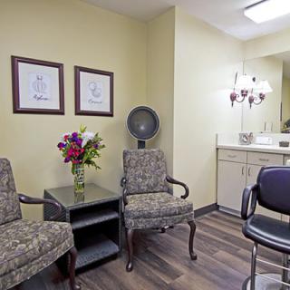 A cozy salon waiting area with chairs, a hair dryer, and a floral arrangement.