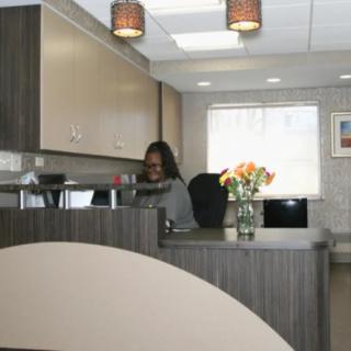 A receptionist is working at a modern office reception desk with a vase of flowers.