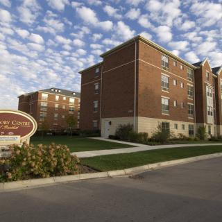 A residential apartment building under a partly cloudy sky with well-kept landscaping and a visible entrance sign.