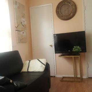 A cozy and modern living room with a black sofa, a television on a stand, wall art, and ample natural light.