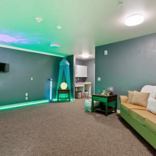 A modern room with ambient green lighting, featuring a couch and wall-mounted television.
