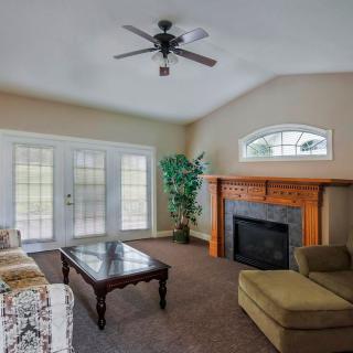 A cozy living room with a sofa, coffee table, and fireplace, featuring large windows and a ceiling fan.