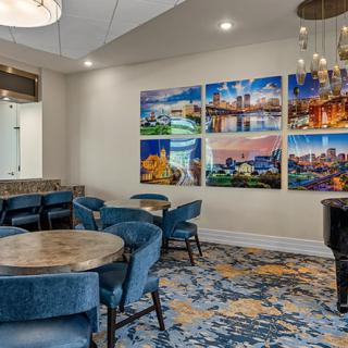 A modern lounge area featuring round tables, blue chairs, vibrant artwork on the wall, and decorative lighting.
