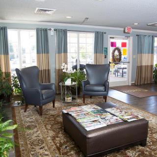 A cozy lobby area featuring comfortable chairs, a coffee table with magazines, and large windows adorned with stylish curtains.