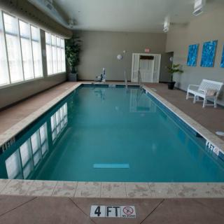 An indoor swimming pool with surrounding tiles, large windows, and a seating area.
