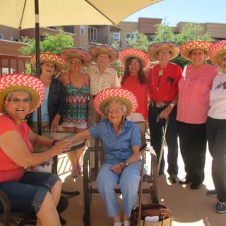 A group of people wearing hats gathered outdoors, smiling and enjoying a sunny day.
