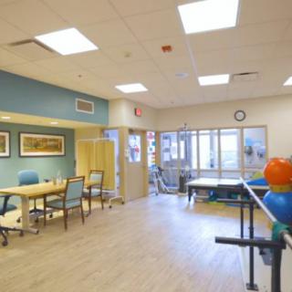 A physical therapy room equipped with tables, chairs, and exercise equipment in a rehabilitation center.