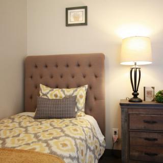 A cozy bedroom with a tufted headboard, decorative pillows, and a warm lamp on the nightstand.