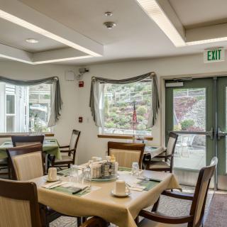 A well-lit dining area with neatly set tables and chairs, featuring large windows and tasteful decor.