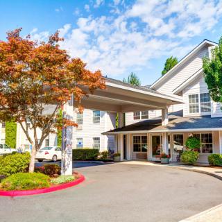 A modern hotel entrance with a landscaped driveway and trees.