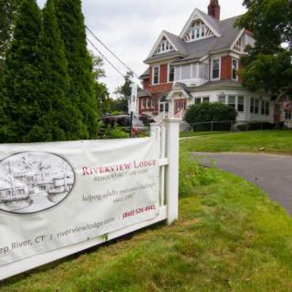 A historic house with a welcoming sign surrounded by greenery.