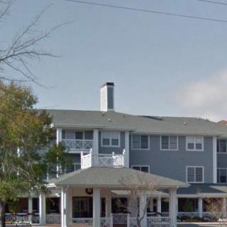 A three-story residential building with a large porch and surrounded by trees on a cloudy day.