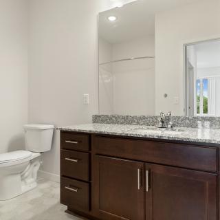 A modern bathroom featuring a granite countertop, large mirror, and dark wood vanity.
