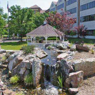 A serene outdoor space featuring a gazebo and a waterfall surrounded by lush greenery.