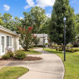 A scenic outdoor pathway bordered by grass and trees, leading past a building and a lamp post.