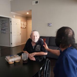 An older adult in a wheelchair is being assisted by a caregiver during mealtime.