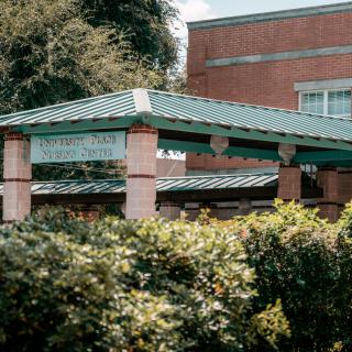 A brick building with a green roof and arches surrounded by lush foliage.