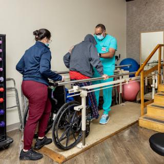 A physical therapy session where a patient is assisted to walk with support.