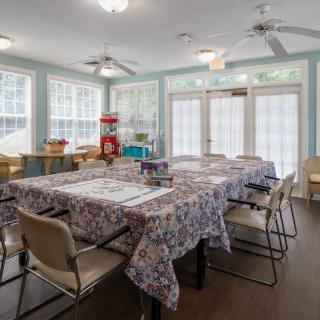 A well-lit craft room with tables and chairs set up for activities, surrounded by large windows.