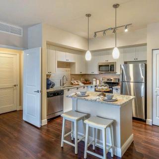 A modern kitchen with an island and stools, featuring stainless steel appliances and stylish lighting.