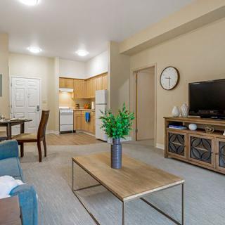 A cozy apartment living room featuring a sofa, coffee table, television, dining area, and a small kitchen.