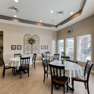 A well-lit dining area featuring multiple tables and chairs, decorated with wall art and large windows.