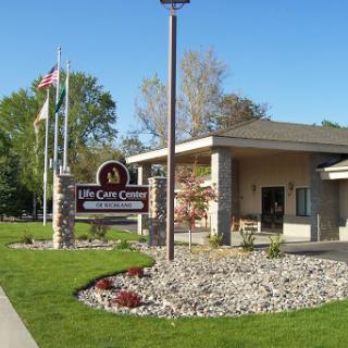The entrance to a community center, featuring well-maintained landscaping and multiple flags.