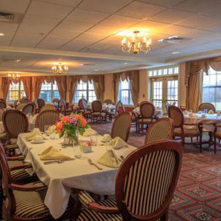 An elegantly decorated dining room with neatly arranged tables and chairs, illuminated by chandeliers.