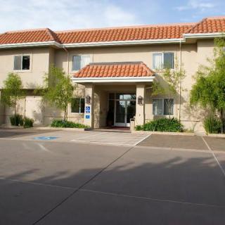 A sunny day view of a two-story building with a red-tiled roof and landscaped entrance.