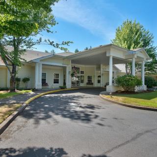 A building entrance with a covered driveway, surrounded by trees and landscaping.