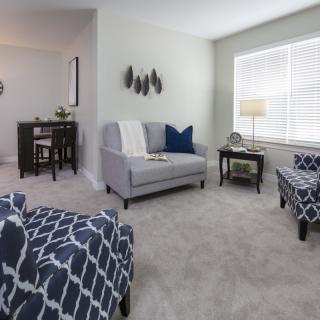 A cozy living room with modern furniture, featuring a sofa, armchairs, and a coffee table under soft natural lighting.